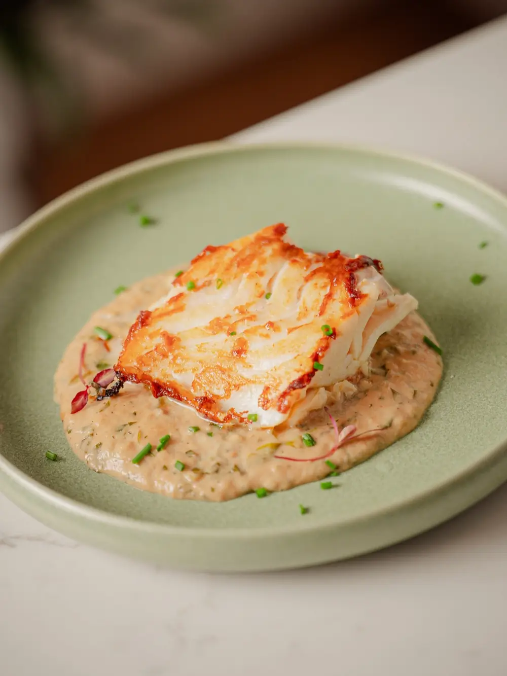 Cod loin on a green plate with a creamy shallot sauce