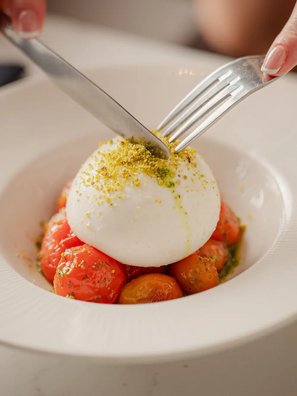 Burrata over confit tomatoes, a knife going in