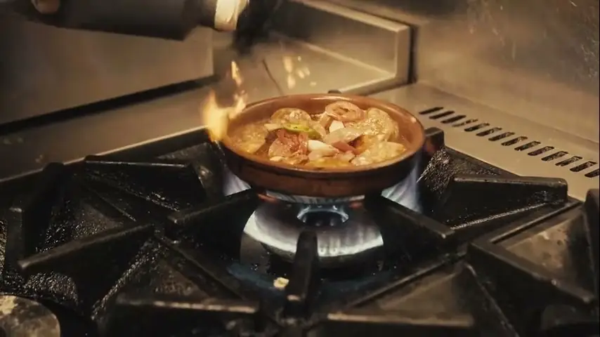 Gambas al pil pil catching flame in a cazuela on the stove